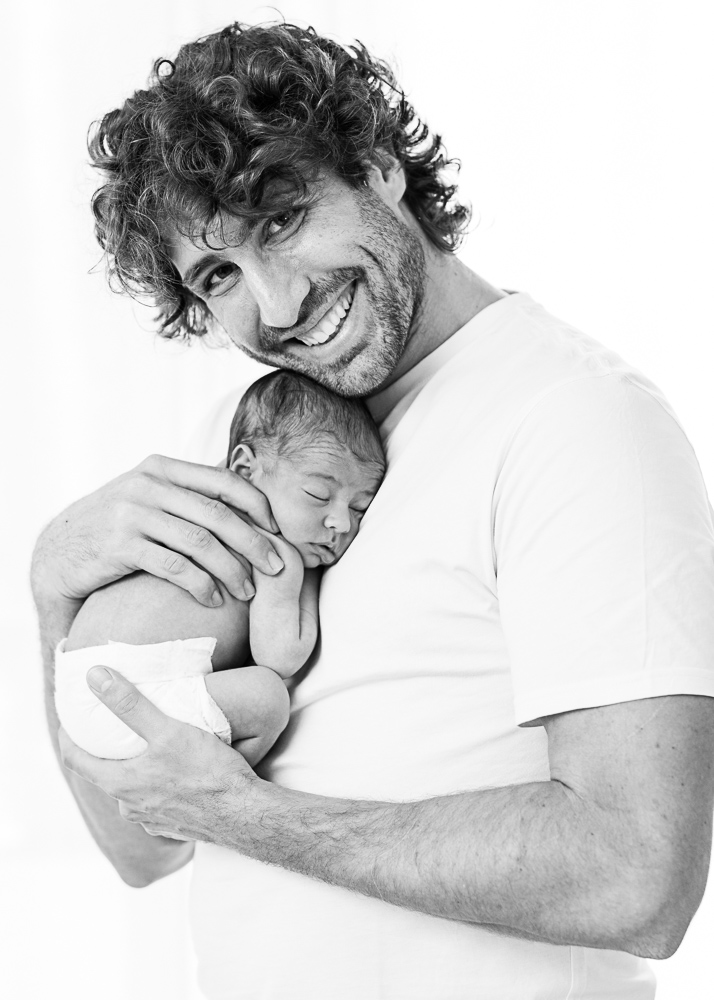 Papa sonrie con su recien nacido en brazos, foto en blanco y negro a contra luz